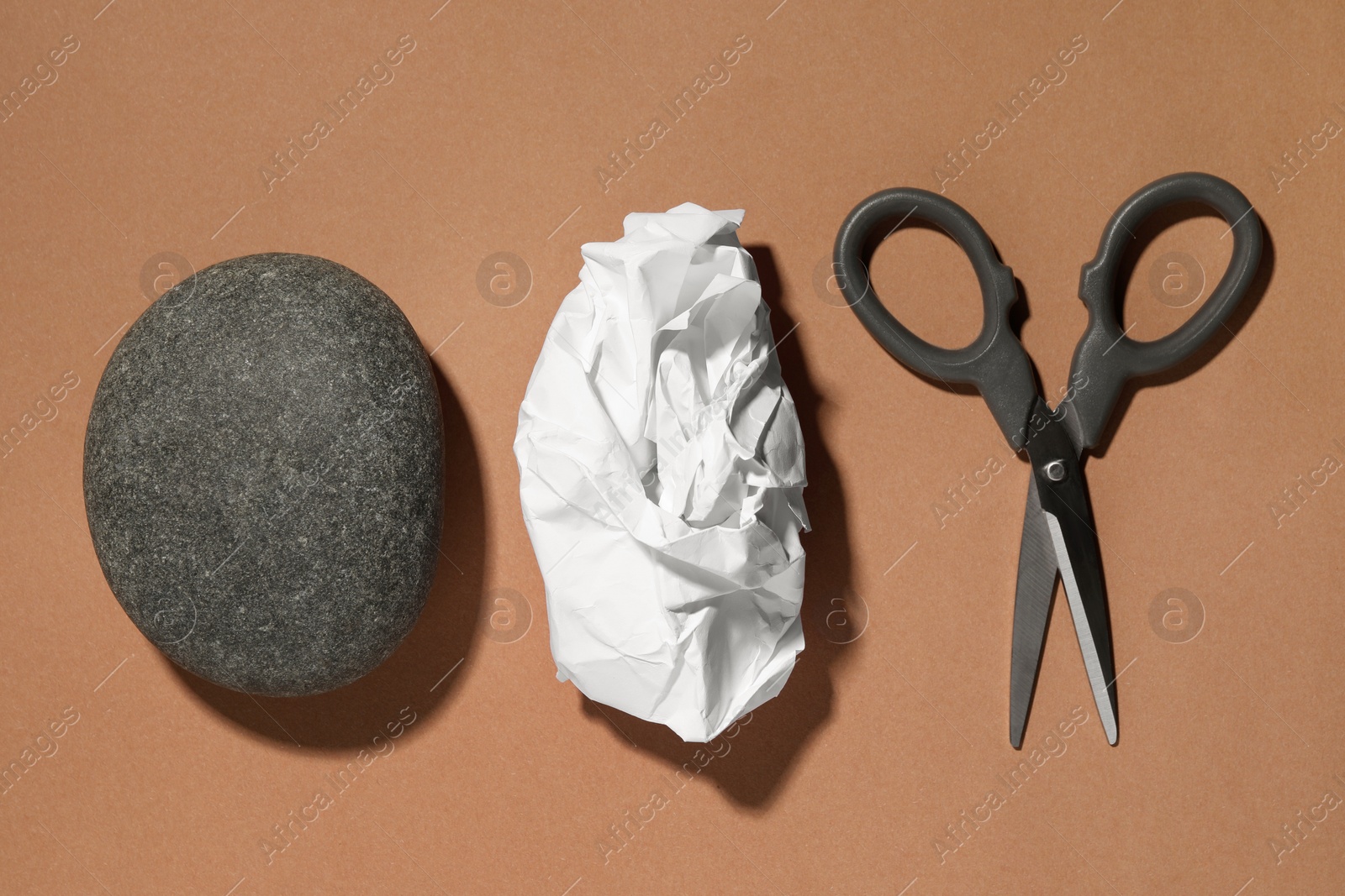 Photo of Rock, crumpled paper and scissors on light brown background, flat lay