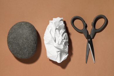 Rock, crumpled paper and scissors on light brown background, flat lay