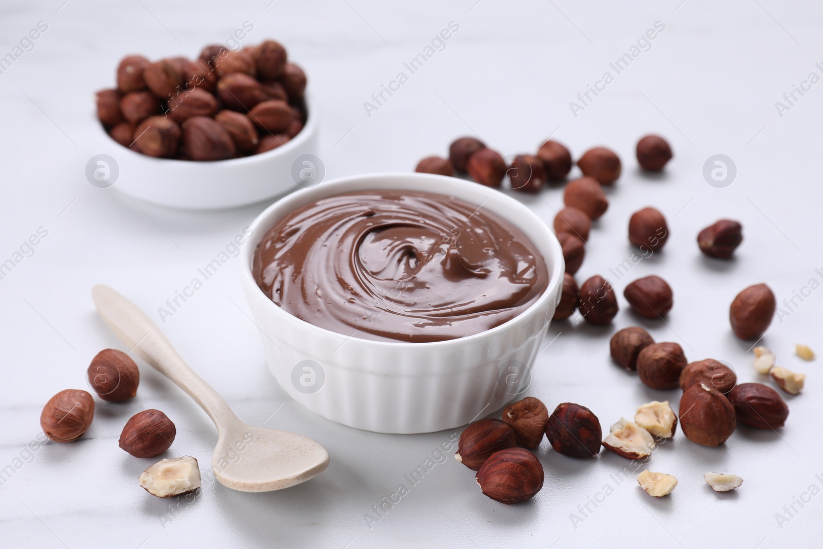 Photo of Bowl with chocolate paste and nuts on white marble table