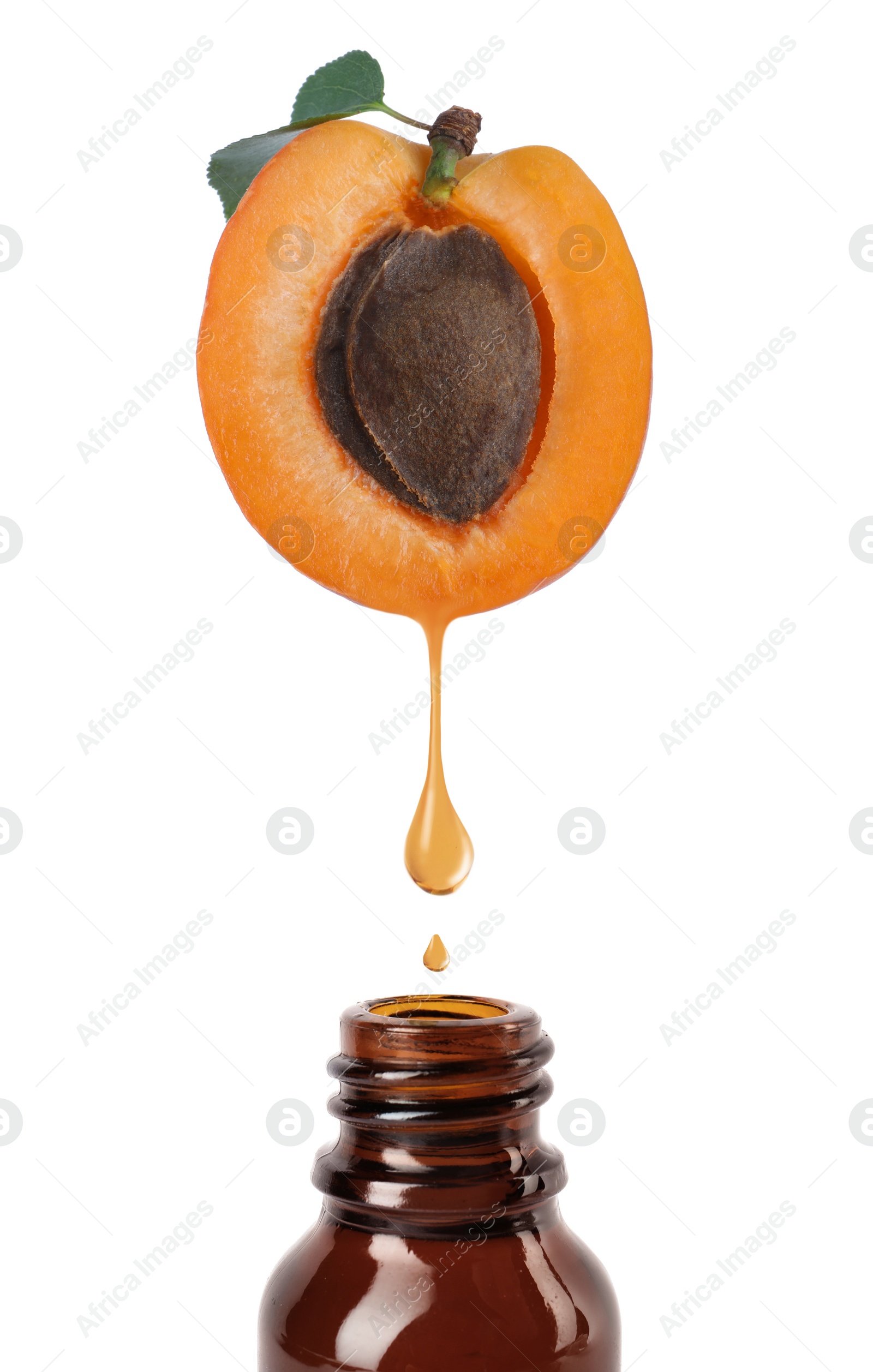 Image of Apricot kernel oil dripping from fresh fruit half into glass bottle on white background