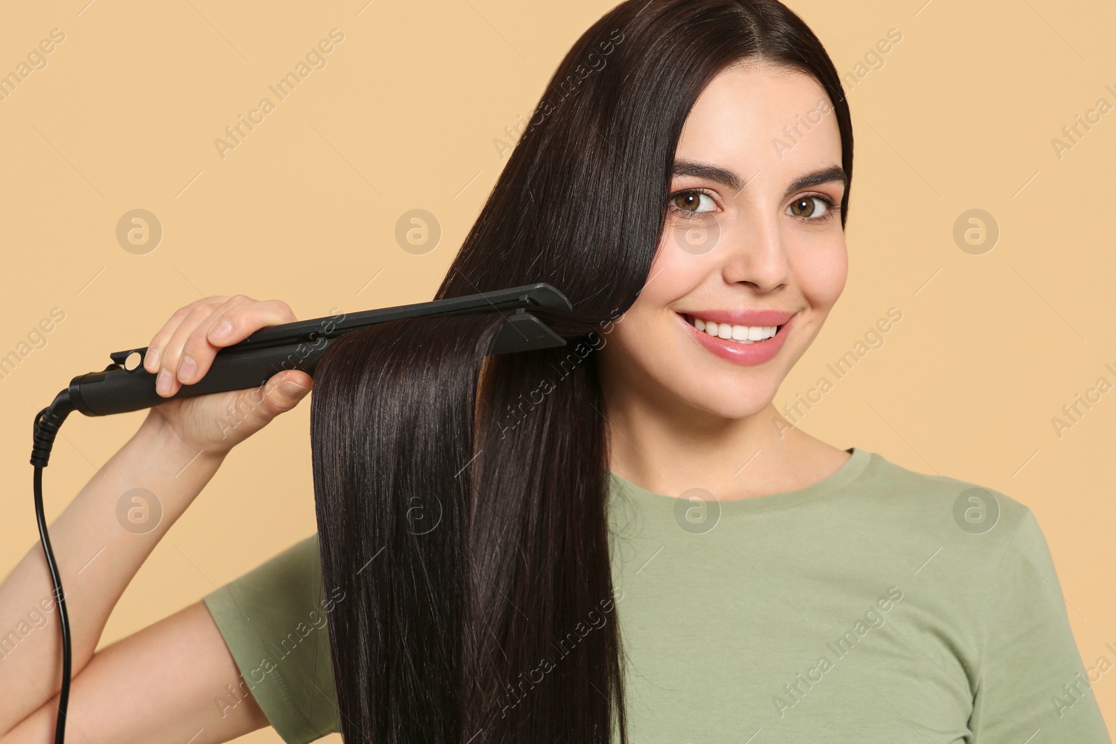 Photo of Beautiful happy woman using hair iron on beige background