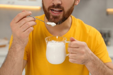 Photo of Man eating delicious yogurt in kitchen, closeup