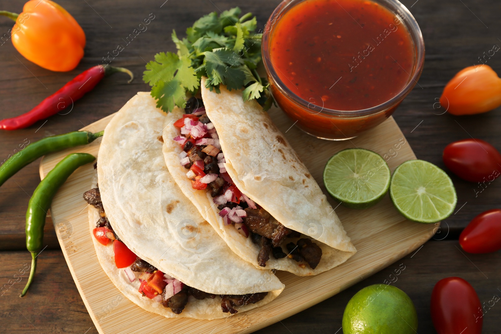 Photo of Delicious tacos with meat, vegetables and sauce on wooden table, above view