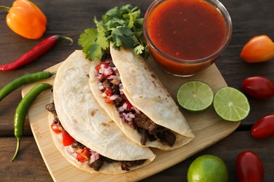Photo of Delicious tacos with meat, vegetables and sauce on wooden table, above view