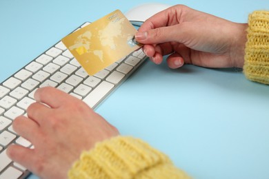Online payment. Woman using credit card and computer keyboard at light blue table, closeup
