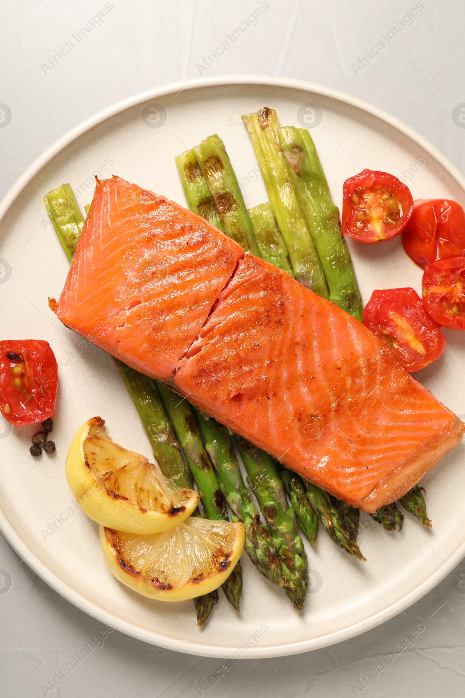 Photo of Tasty grilled salmon with asparagus, tomatoes, spices and lemon on light grey table, top view