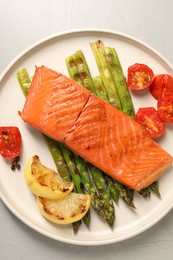 Photo of Tasty grilled salmon with asparagus, tomatoes, spices and lemon on light grey table, top view