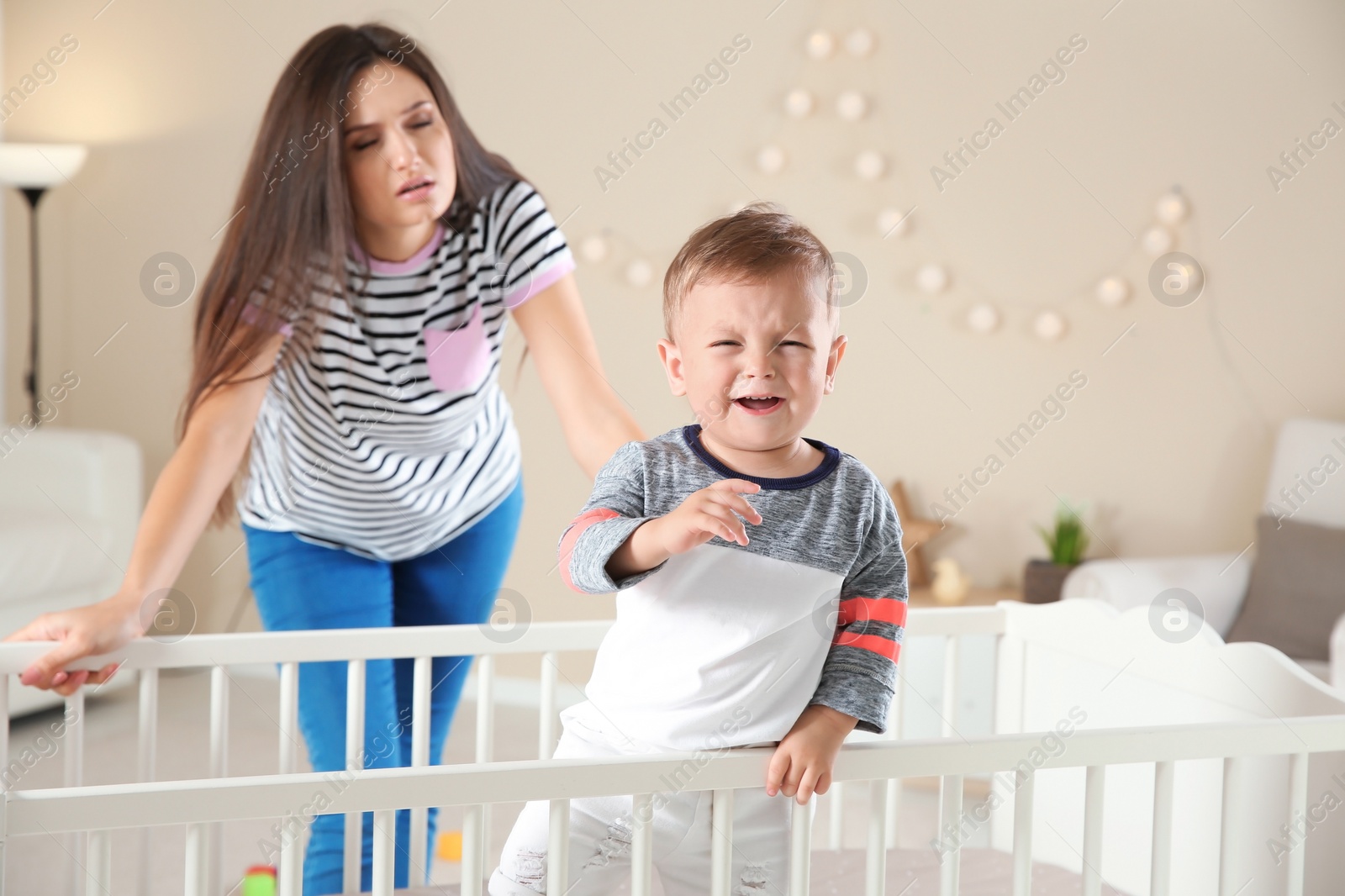 Photo of Crying baby boy in crib and young mother suffering from postnatal depression at home