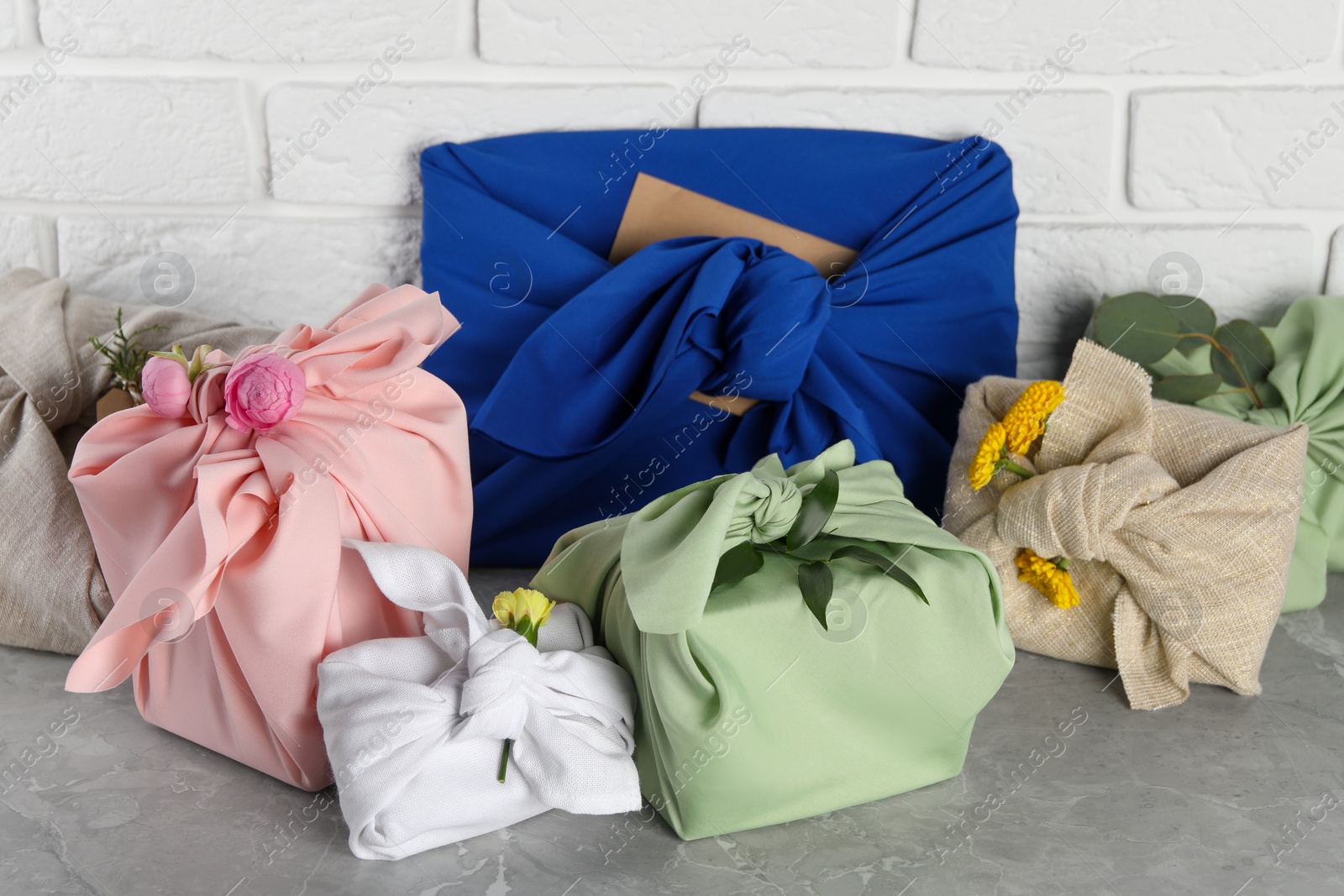 Photo of Furoshiki technique. Many gifts packed in fabric on grey table