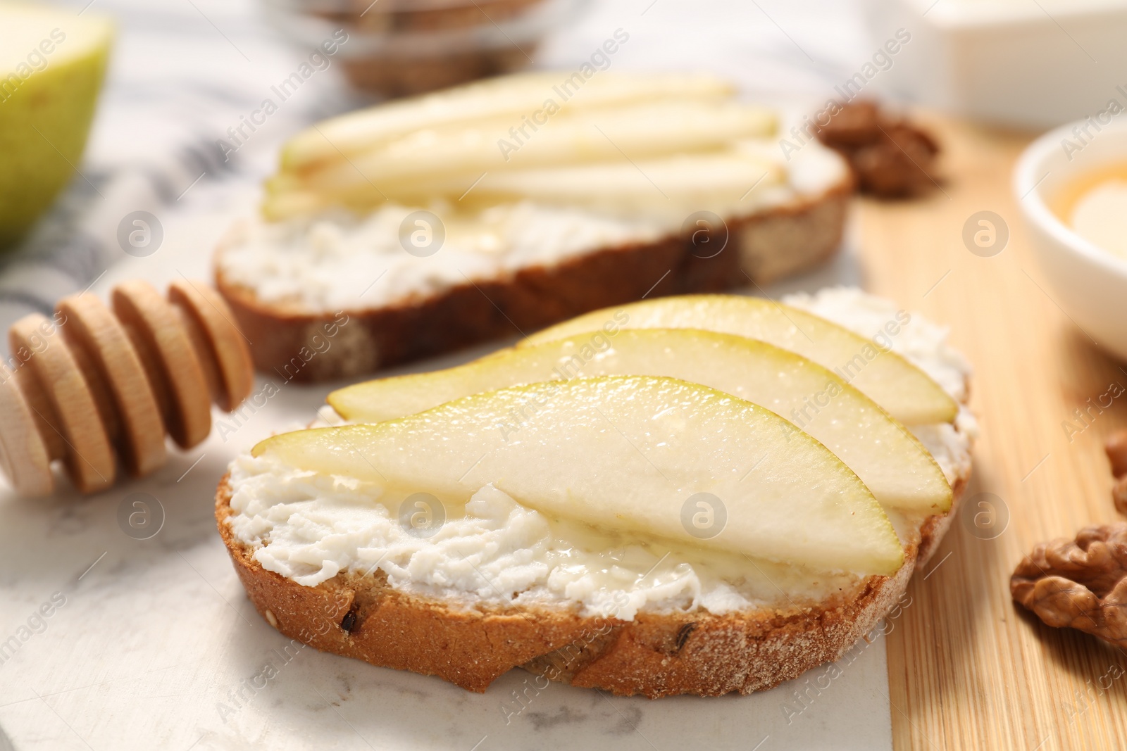 Photo of Delicious ricotta bruschettas with pear and walnut on white table, closeup