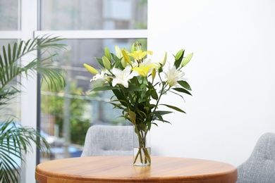 Photo of Vase with bouquet of beautiful lilies on wooden table indoors