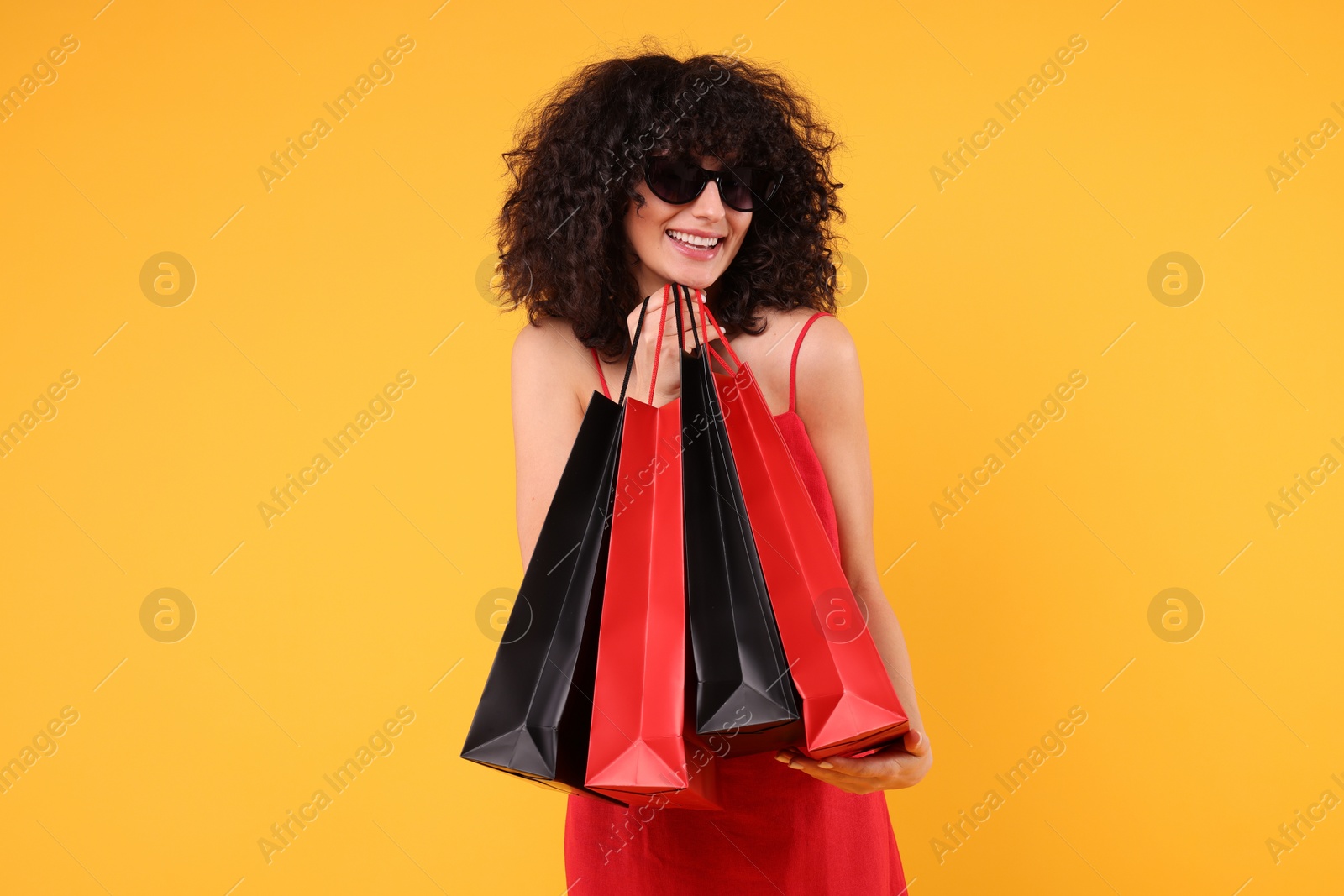 Photo of Happy young woman with shopping bags and stylish sunglasses on yellow background