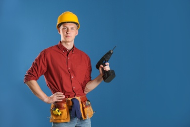 Handsome young working man with electric drill against color background, space for text