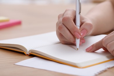 Woman writing in notebook at wooden table indoors, closeup