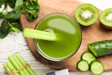 Glass of celery juice and fresh ingredients on white wooden table, flat lay