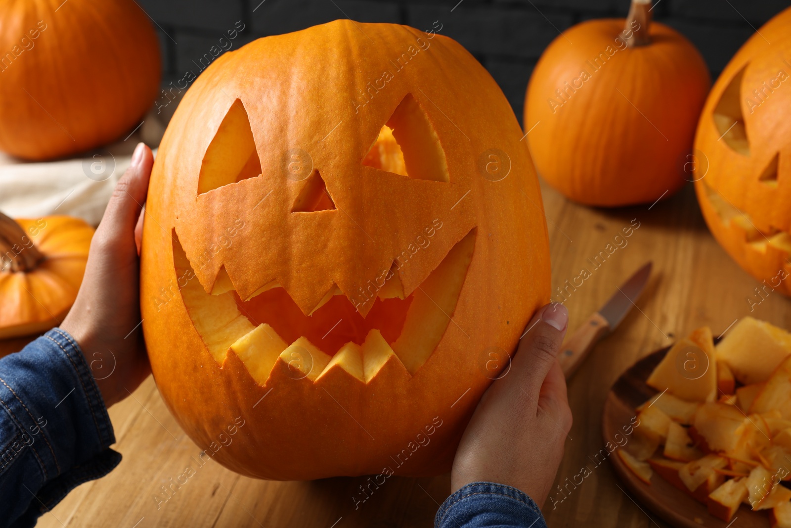 Photo of Woman with carved pumpkins at wooden table, closeup. Halloween celebration