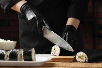 Chef in gloves cutting sushi roll at table, closeup