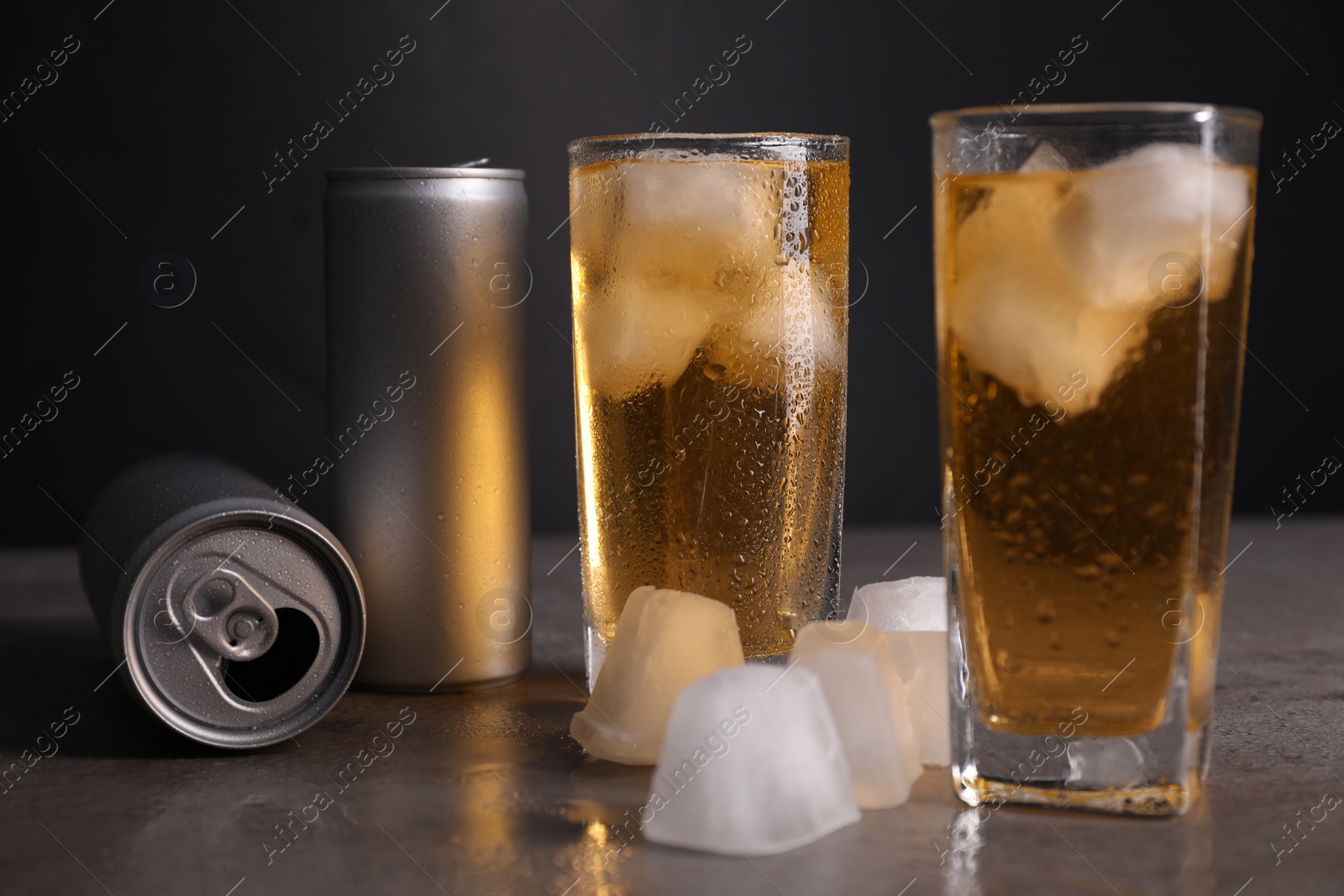 Photo of Tasty energy drink with ice cubes in glasses and aluminium cans on grey table, closeup