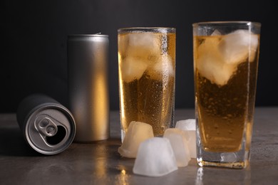 Photo of Tasty energy drink with ice cubes in glasses and aluminium cans on grey table, closeup