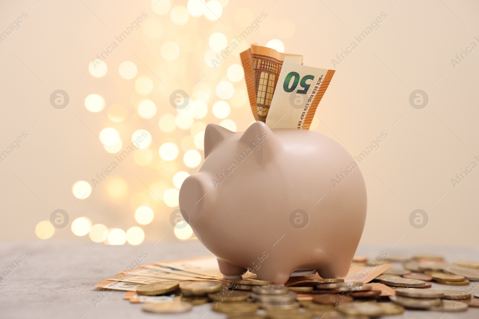 Photo of Piggy bank with euro banknote and coins on grey table against blurred lights