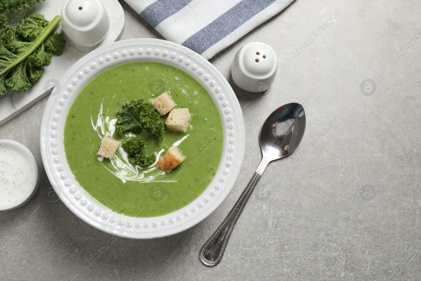 Photo of Tasty kale soup with croutons served on grey table, flat lay