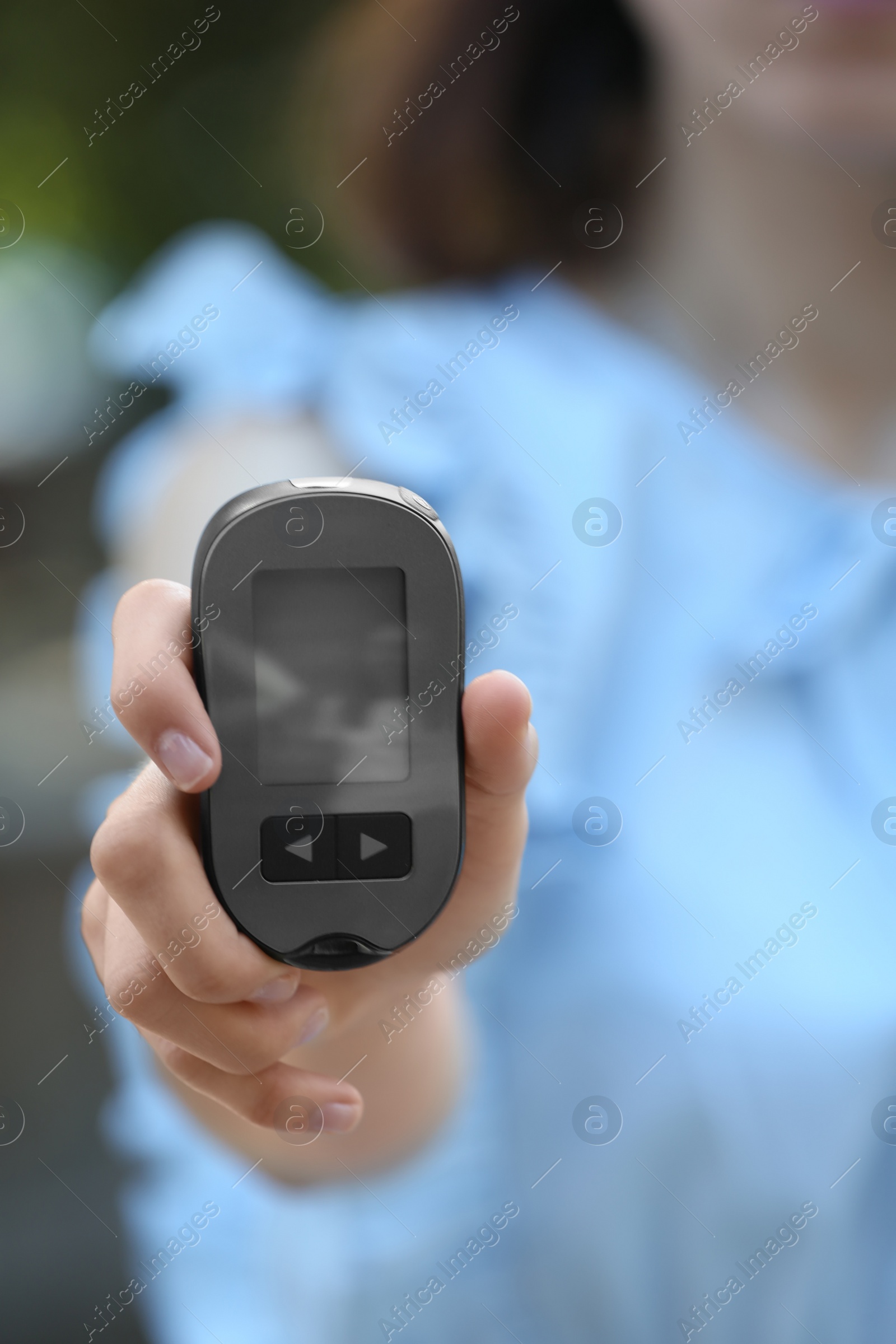 Photo of Woman holding digital glucometer on blurred background. Diabetes control