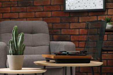 Photo of Stylish turntable with vinyl record, headphones and houseplant on table indoors