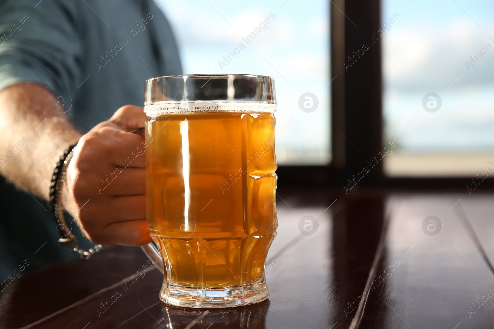 Photo of Man with glass of tasty beer at wooden table in pub, closeup. Space for text