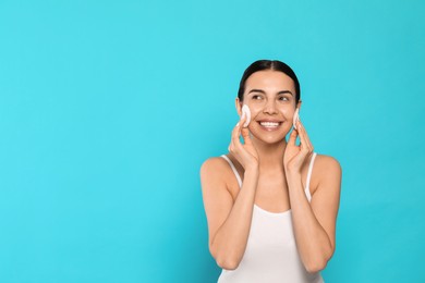 Young woman using cotton pads with micellar water on light blue background, space for text