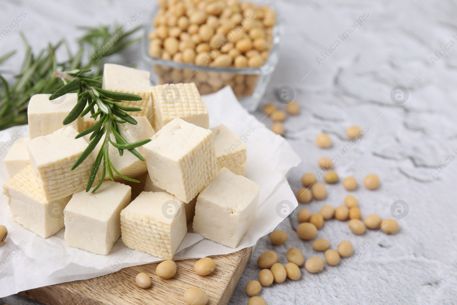 Photo of Delicious tofu cheese, rosemary and soybeans on light gray textured table, closeup