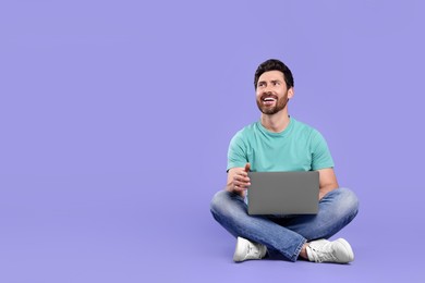 Photo of Happy man with laptop on purple background. Space for text