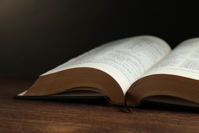 Open hardcover Bible on wooden table, closeup. Religious book