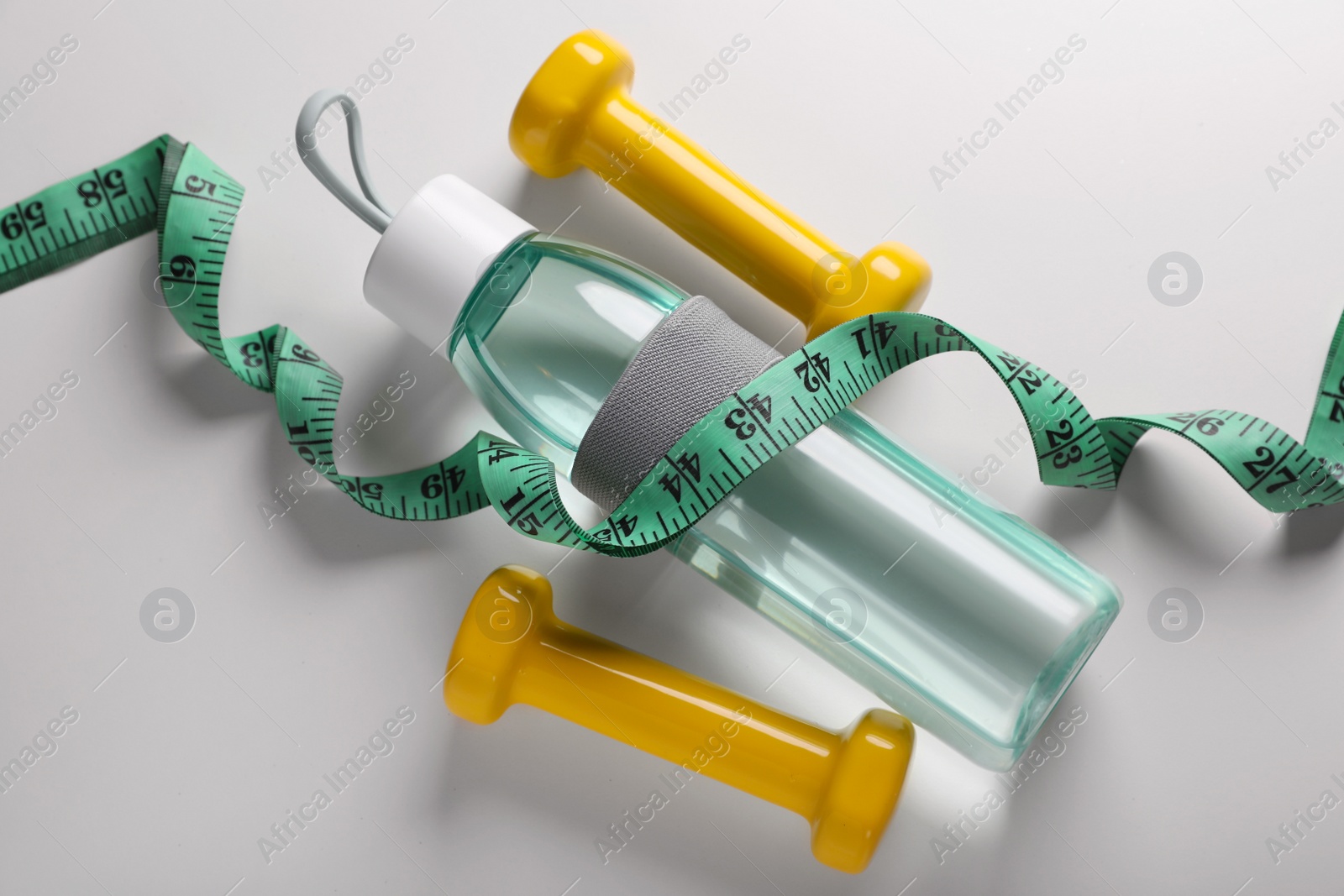 Photo of Measuring tape, dumbbells and bottle with water on white background, above view. Weight control concept