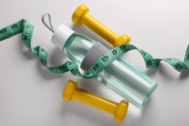 Photo of Measuring tape, dumbbells and bottle with water on white background, above view. Weight control concept