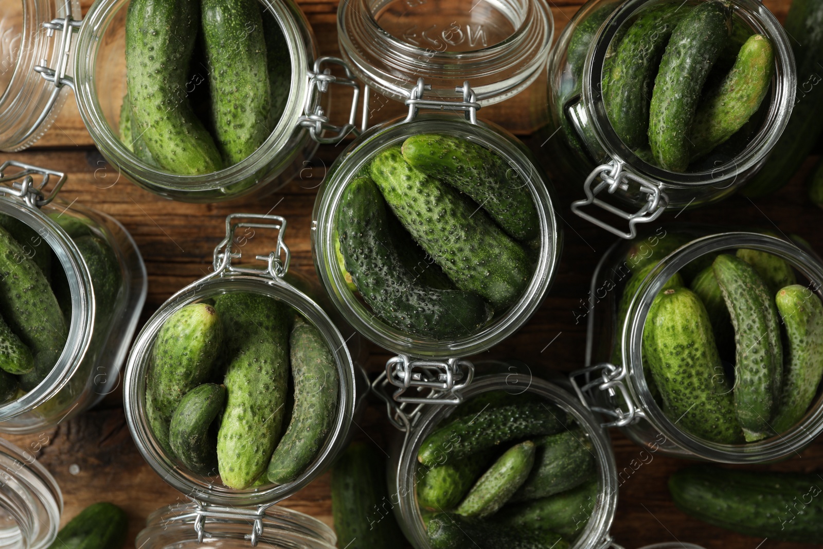 Photo of Pickling jars with fresh cucumbers on wooden table, flat lay