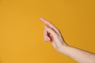 Woman pointing at something on yellow background, closeup. Finger gesture