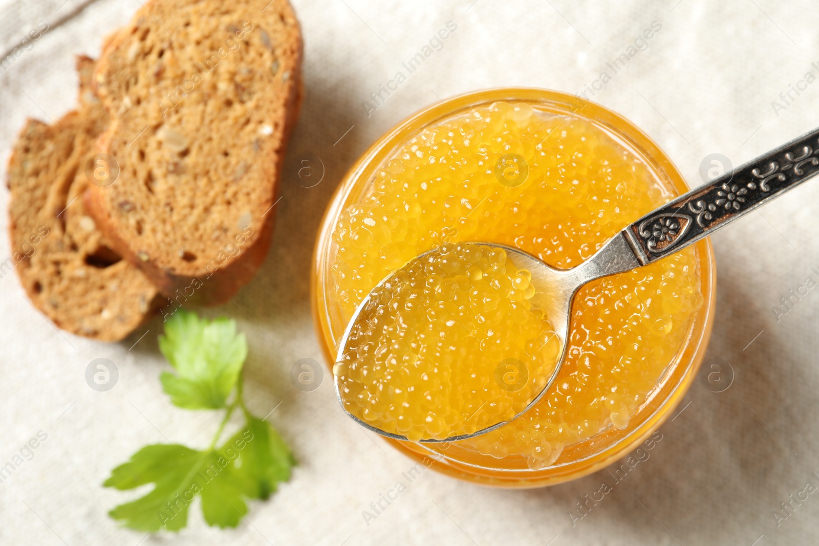 Photo of Fresh pike caviar in glass jar, bread and parsley on table, flat lay