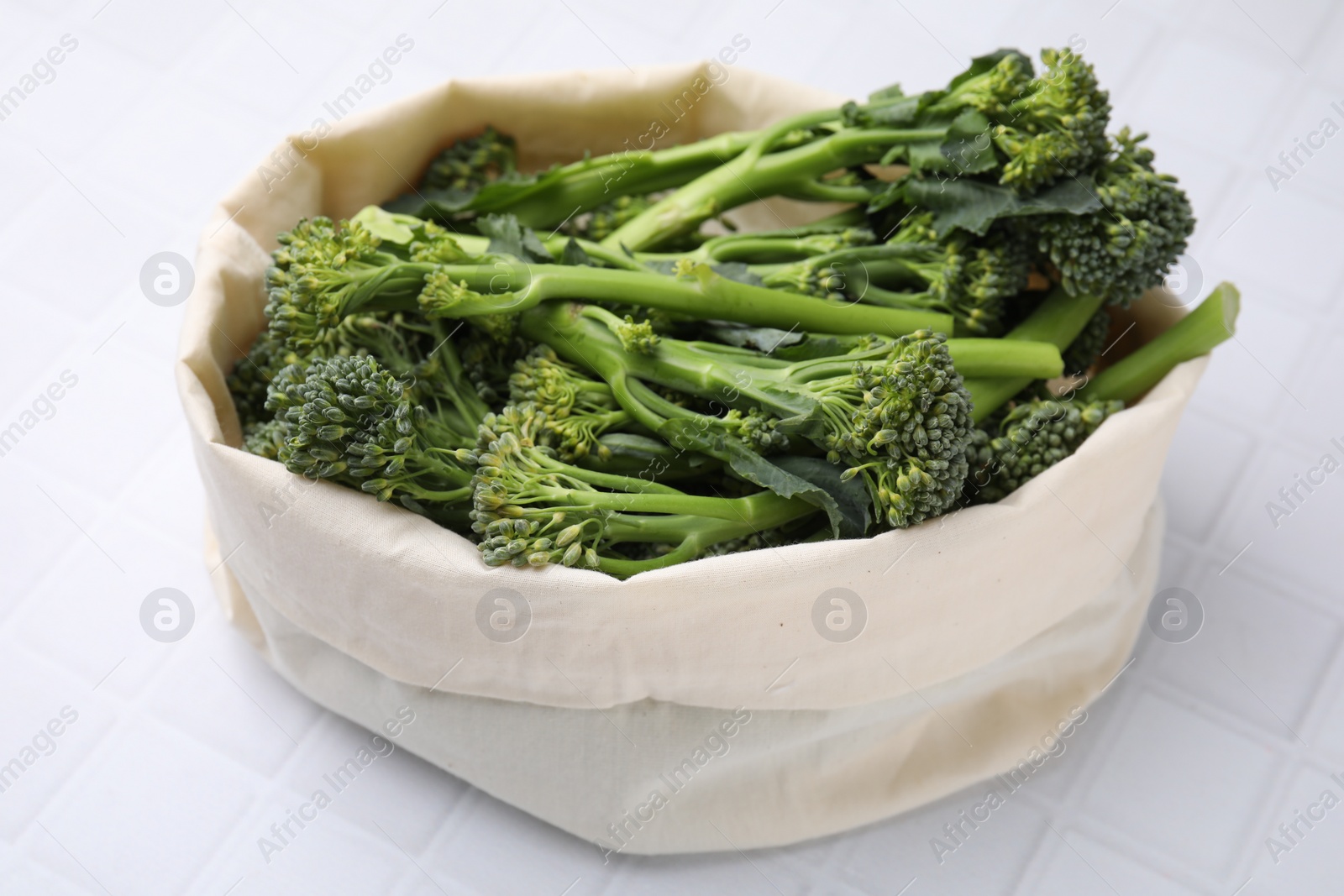 Photo of Bag with fresh raw broccolini on white tiled table, closeup. Healthy food