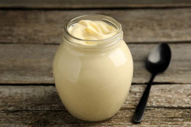 Jar of delicious mayonnaise and spoon on wooden table