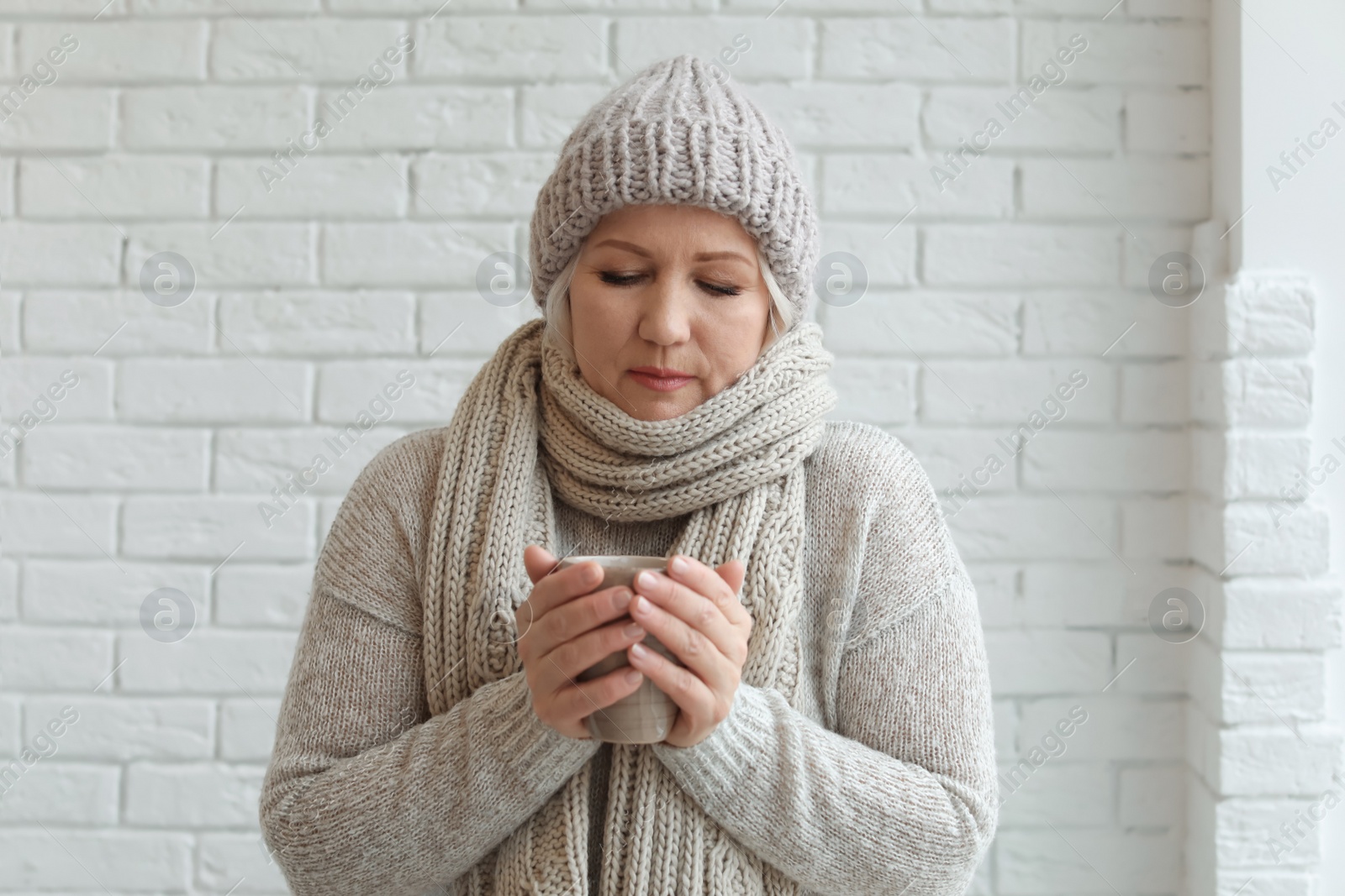 Photo of Mature woman in warm clothes suffering from cold on brick background