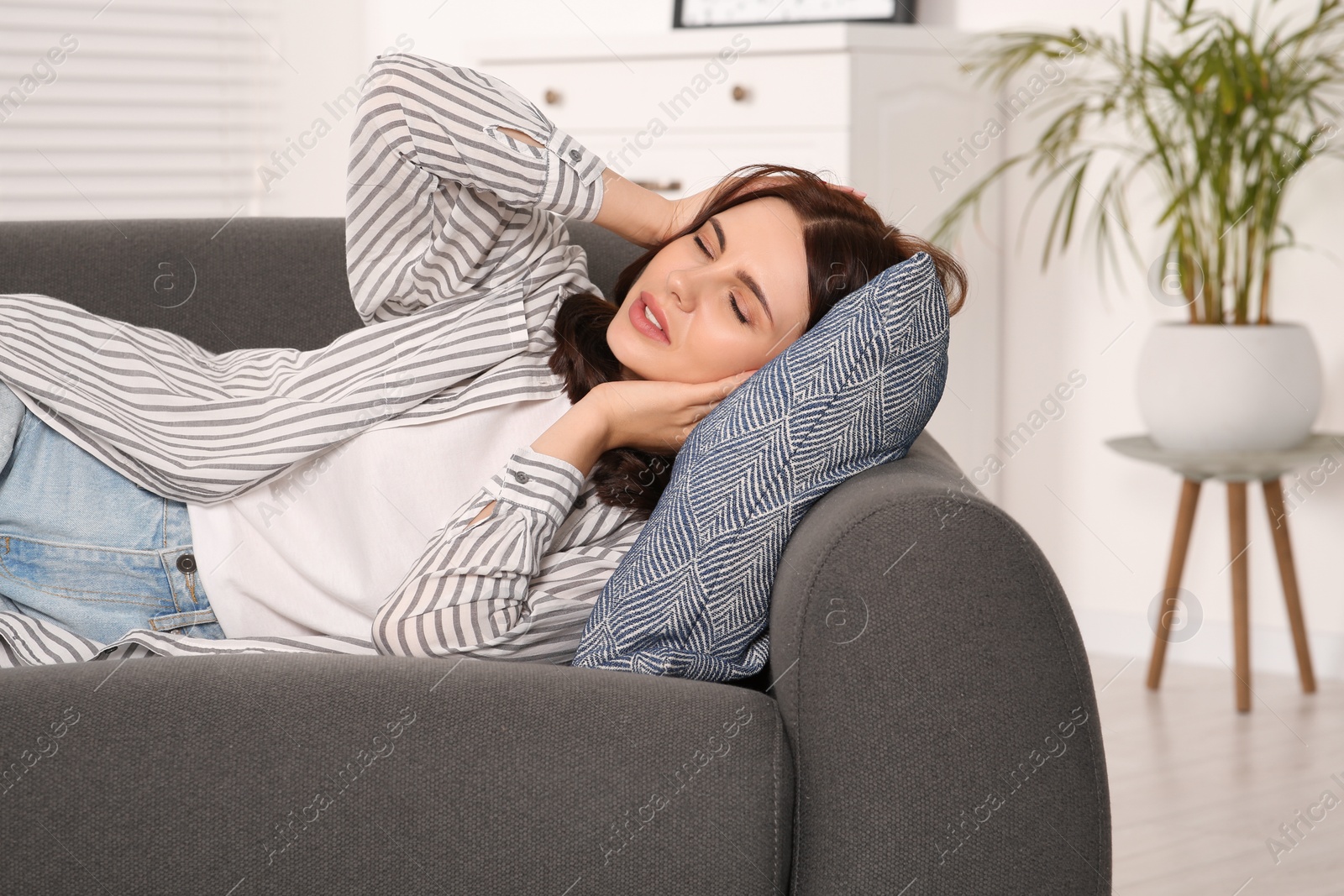 Photo of Young woman suffering from headache on sofa indoors. Hormonal disorders