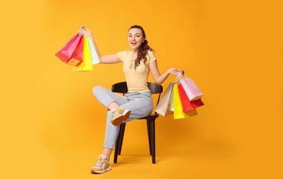 Photo of Happy woman holding colorful shopping bags on chair against orange background
