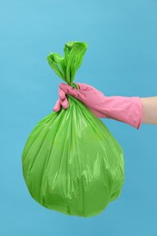 Photo of Woman holding plastic bag full of garbage on light blue background, closeup