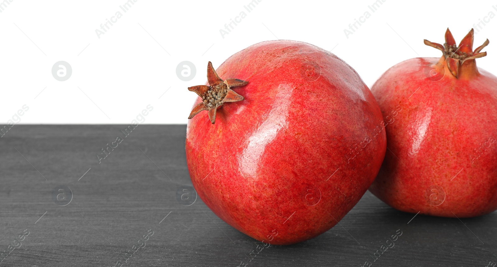 Photo of Fresh pomegranates on black wooden table against white background, space for text