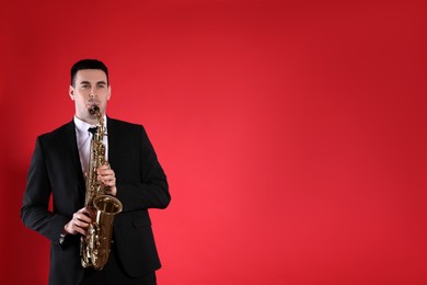 Young man in elegant suit playing saxophone on red background. Space for text