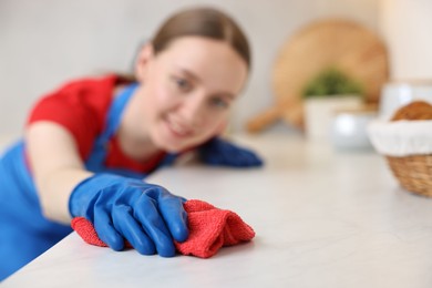 Woman cleaning white countertop with rag in kitchen, selective focus