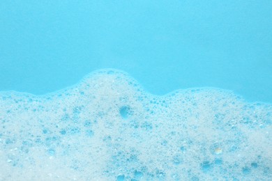 Photo of Fluffy bath foam on turquoise background, top view. Space for text