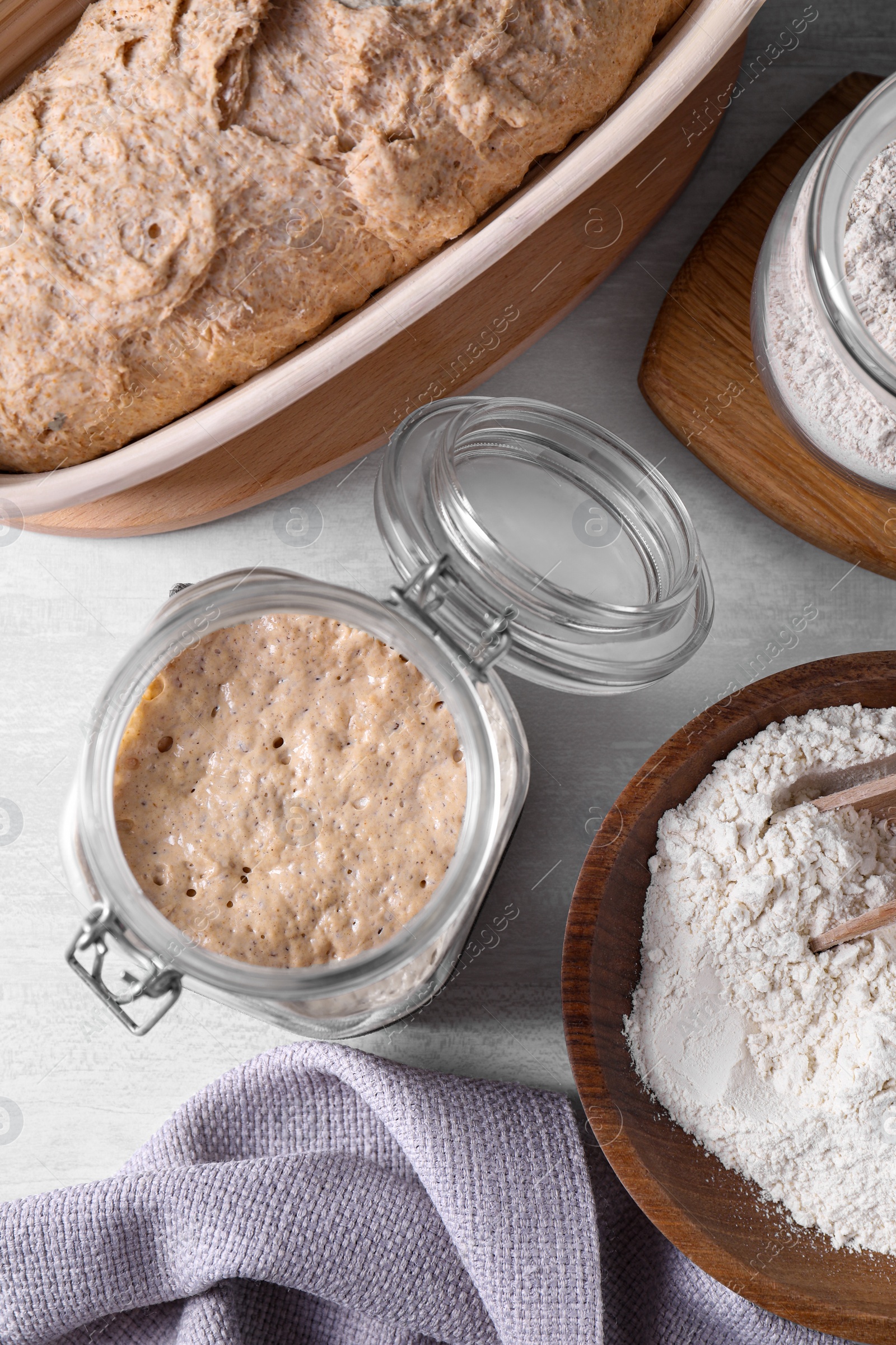 Photo of Sourdough starter in glass jar, flour and dough on light table, flat lay