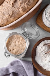 Sourdough starter in glass jar, flour and dough on light table, flat lay