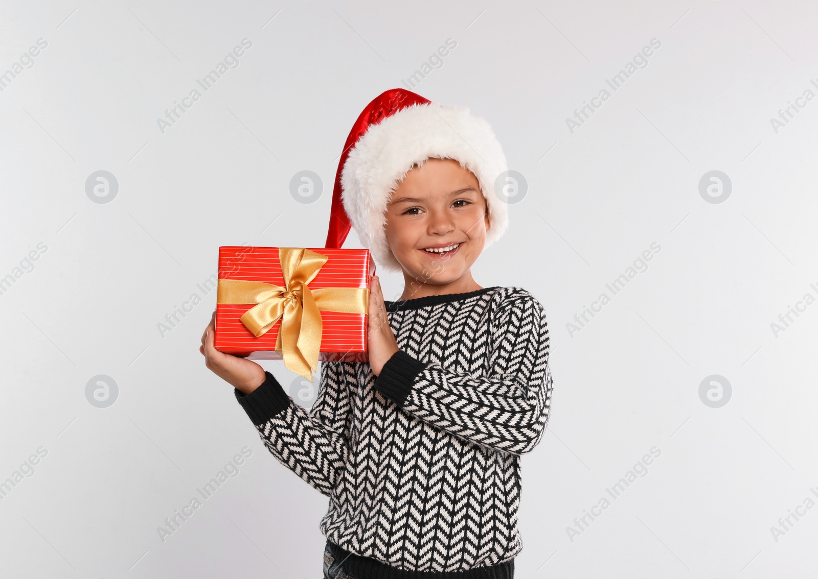 Photo of Happy little child in Santa hat with gift box on light grey background. Christmas celebration